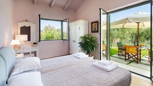 Een slaapkamer met twee bedden, een bureau, een stoel, een spiegel en een grote schuifglazen deur die leidt naar een terras buiten met een tafel en stoelen.
