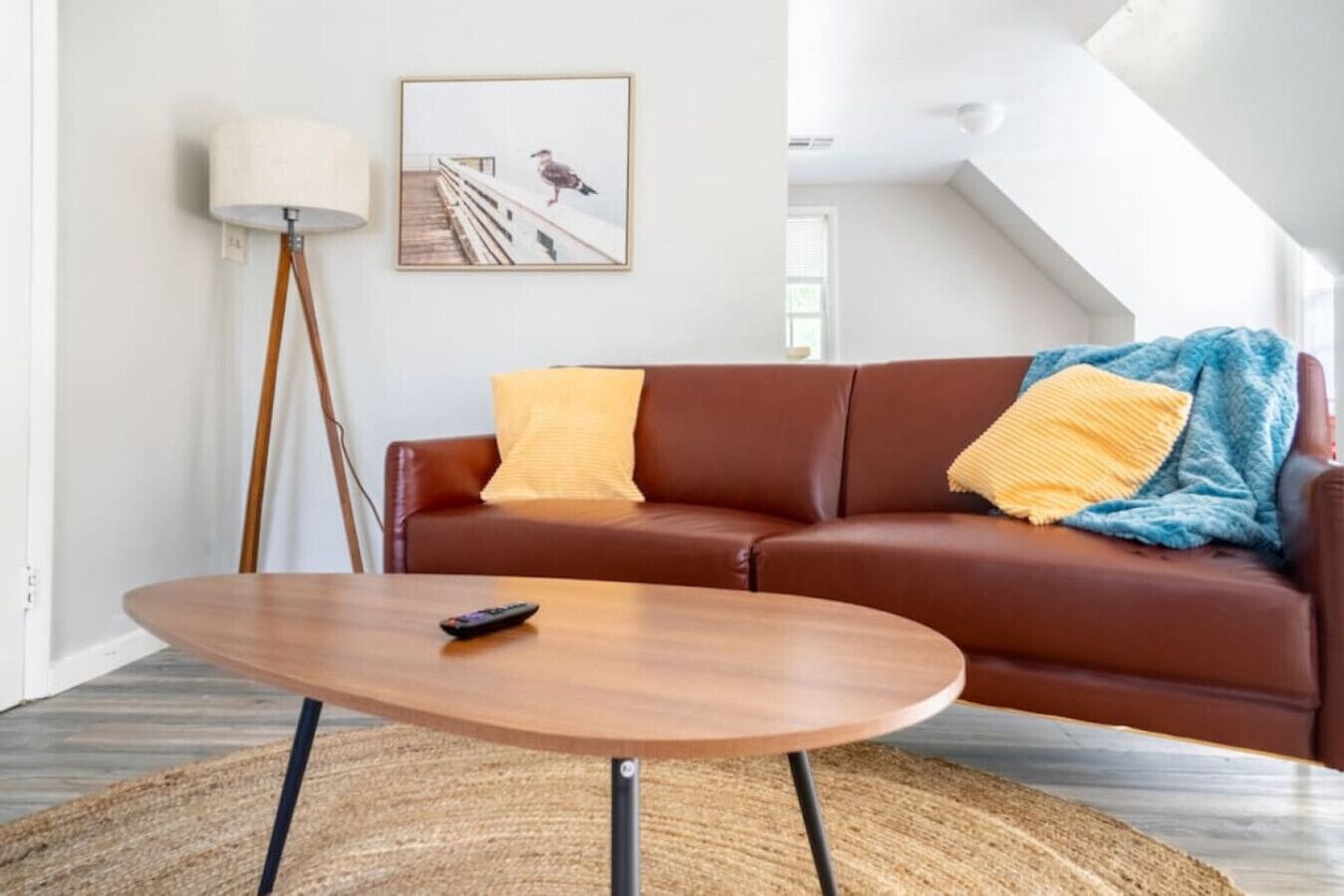 A living room with a brown leather sofa, a round wooden coffee table, a floor lamp, and a framed picture on the wall.