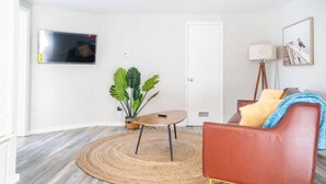 A living room with a round coffee table, a red leather sofa, a potted plant, and a mounted TV. - OKC 9 · Charming Carriage Cottage from 1920`s! (Oklahoma City)