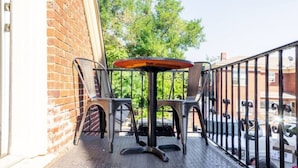 A small outdoor seating area with a table and chairs, a brick wall, and a metal railing. - OKC 9 · Charming Carriage Cottage from 1920`s! (Oklahoma City)