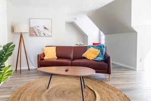En moderne stue med en brun lædersofa, et rundt sofabord og en stor plante.