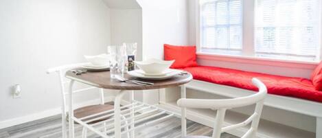 A dining area with a table and chairs, a window with a red cushion, and a view of the city.