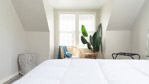 A bedroom with a large bed, a chair, a potted plant, and a window with blinds. - OKC 9 · Charming Carriage Cottage from 1920`s! (Oklahoma City)