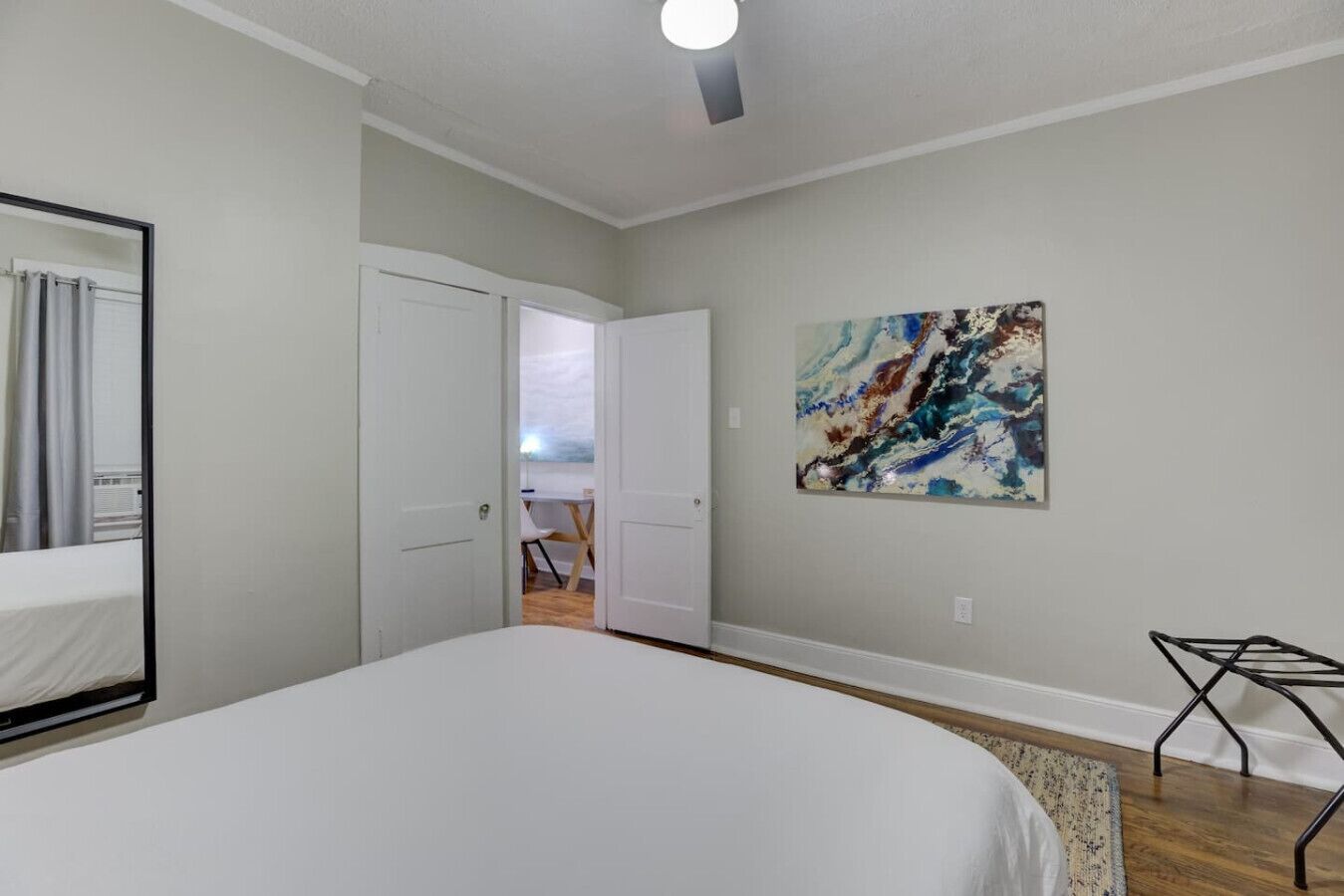 Een slaapkamer met een groot bed, een deur naar een andere kamer en een kleurrijk abstract schilderij aan de muur.