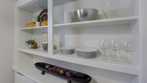 A kitchen with white cabinets, a black tray with decorative items, and various kitchenware including plates, bowls, and wine glasses.
