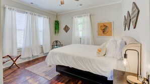 A bedroom with a bed, a ceiling fan, a desk with a lamp, and a chair.