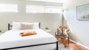A bedroom with a bed, a chair, a small table, and a painting on the wall.