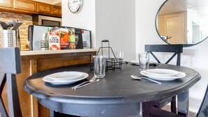 A dining table with plates, cutlery, and glasses, a clock, and a magazine rack with cookbooks.