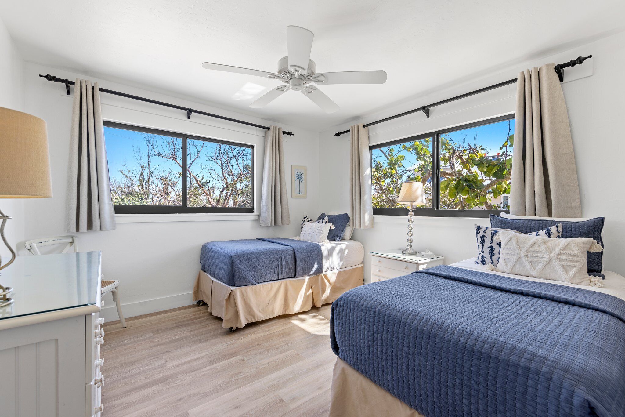 A bedroom with two beds, a ceiling fan, and large windows.