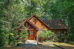 Une cabane en bois dotée d’un porche à l’avant, entourée d’une forêt dense.