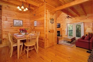 A wooden cabin interior with a dining area, a living room, and a fireplace. - Sweet Pickins-1 Bedroom 2 Beds 1 Bathroom (Gatlinburg)