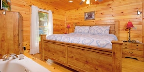 A wooden cabin bedroom with a bed, bedside lamps, a wooden wardrobe, and a window with curtains.