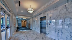 Um corredor com piso de mármore, um elevador e uma porta que dá para um quarto.