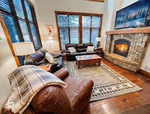 A cozy living room with leather sofas, a fireplace, and large windows.