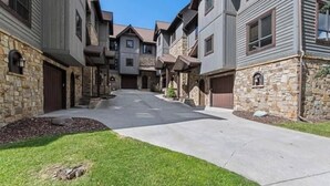 A residential street with multi-story houses, stone foundations, and a clear sky. - Luxury Home | Hot Tub | Ski In / Ski Out | Warmers (Whitefish)