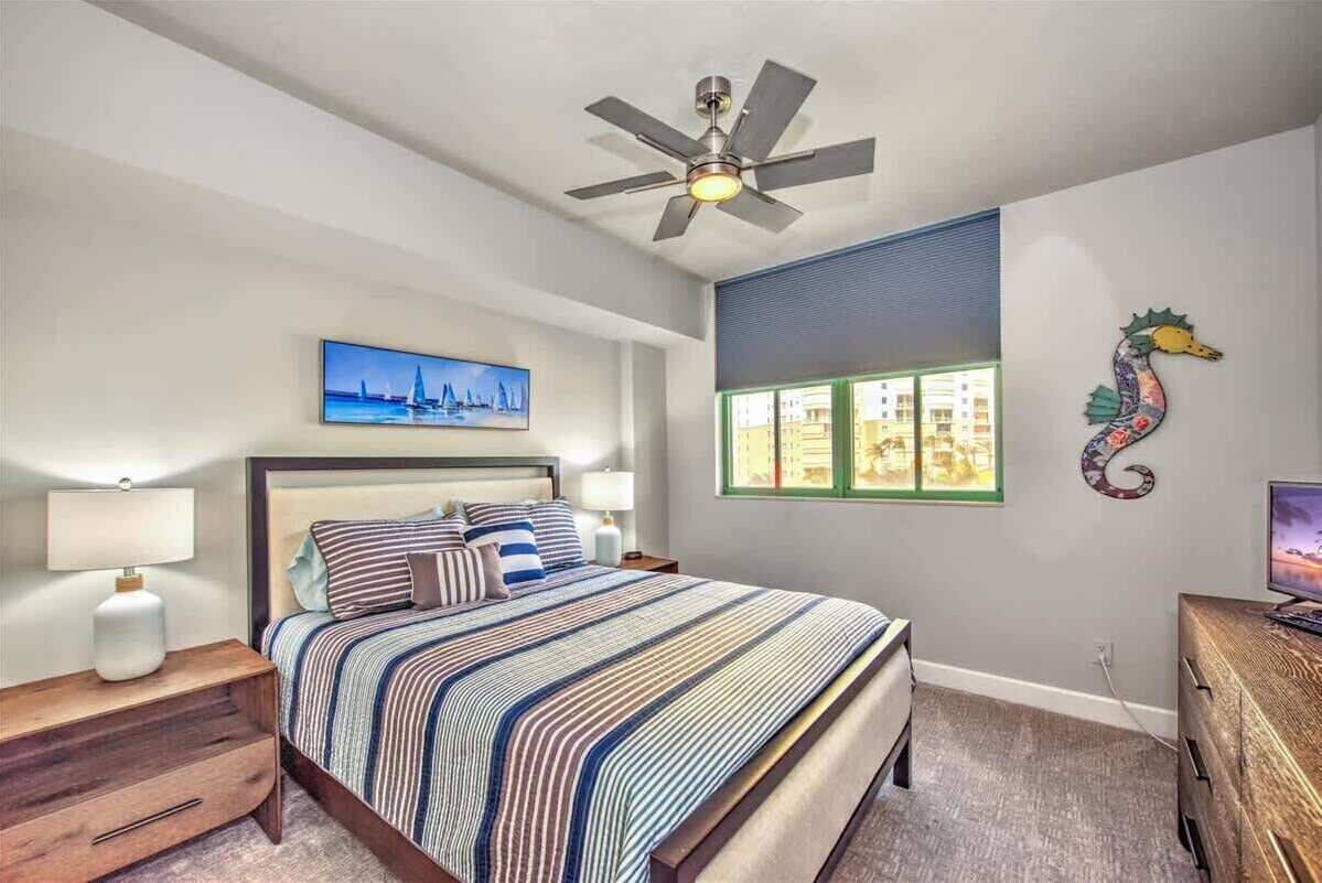 Una camera da letto con un letto, comodini, una ventola a soffitto, una finestra con vista e un riccio di mare decorativo sulla parete.