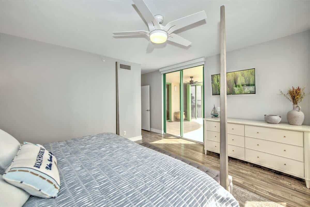 Een moderne slaapkamer met een bed, een plafondventilator, een dressoir en een schuifdeur naar een balkon.