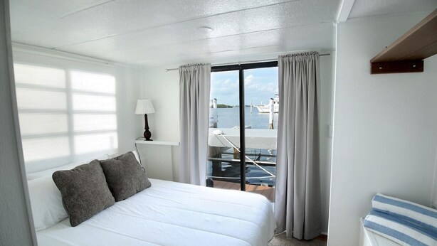 A hotel room with a bed, a lamp, and a view of boats through the window. - Aqua Lodge Houseboat "Sea Turtle" (Tavernier)