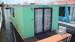 A small, green boat named 'Sea Turtle' docked at a marina with a wooden deck and a covered entrance. - Aqua Lodge Houseboat "Sea Turtle" (Tavernier)