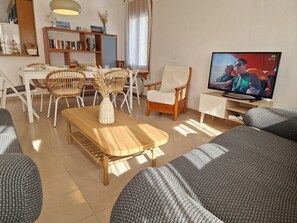 A living room with a wooden table, wicker chairs, a sofa, a television, and a bookshelf.