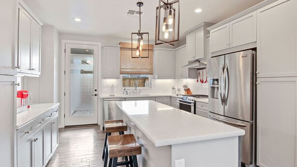 A modern kitchen with white cabinetry, a large island with stools, stainless steel appliances, and pendant lighting. - A diamond in the rough (Rocklin)