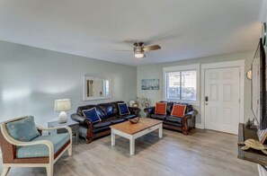 A living room with a ceiling fan, two leather sofas with colorful cushions, a wooden coffee table, and a light-colored armchair.