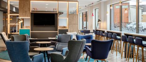 A modern lounge area with seating, a TV, and a bar with stools.