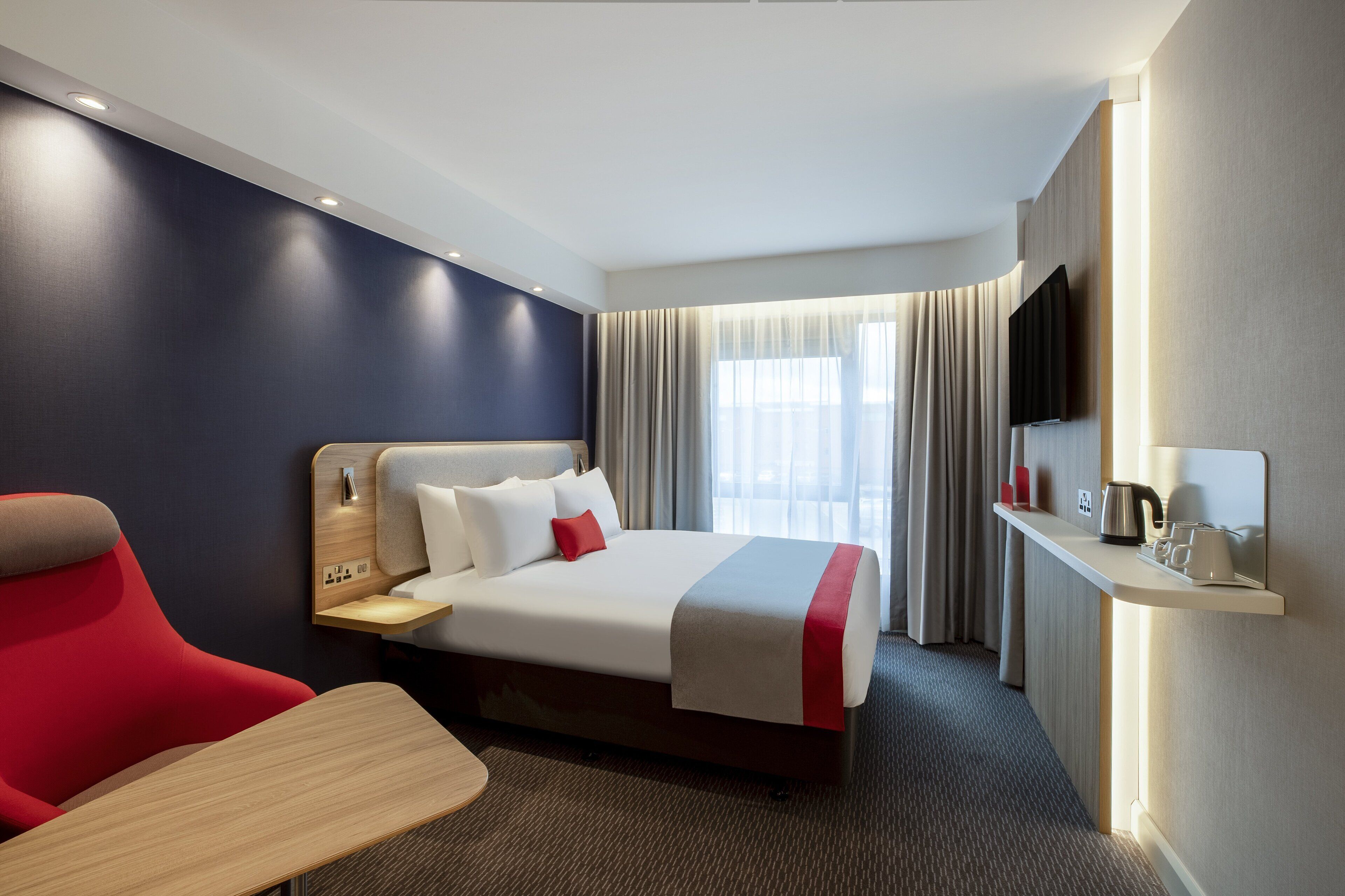 A hotel room with a bed, a desk, a chair, a TV, and a window with curtains.