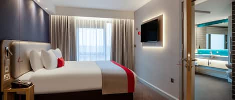 A modern hotel room with a bed, a TV, a bathroom visible through an open door, and a window with curtains.
