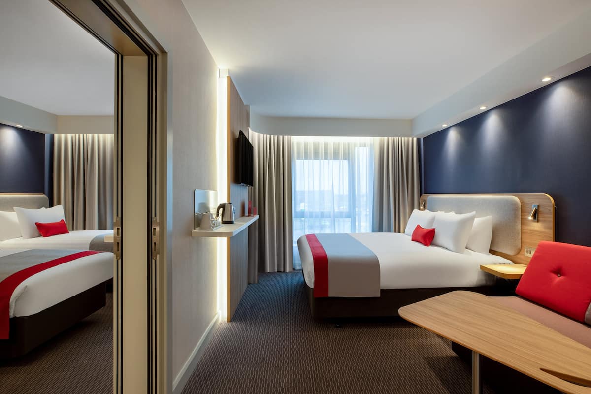 A hotel room with two beds, a desk, a TV, and a window with curtains.