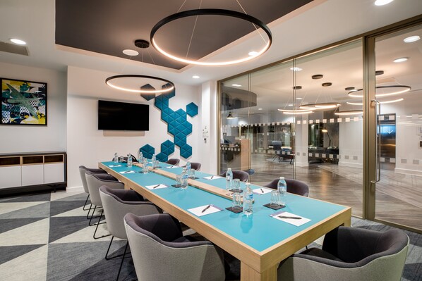 A conference room with a long table, chairs, and a glass partition.