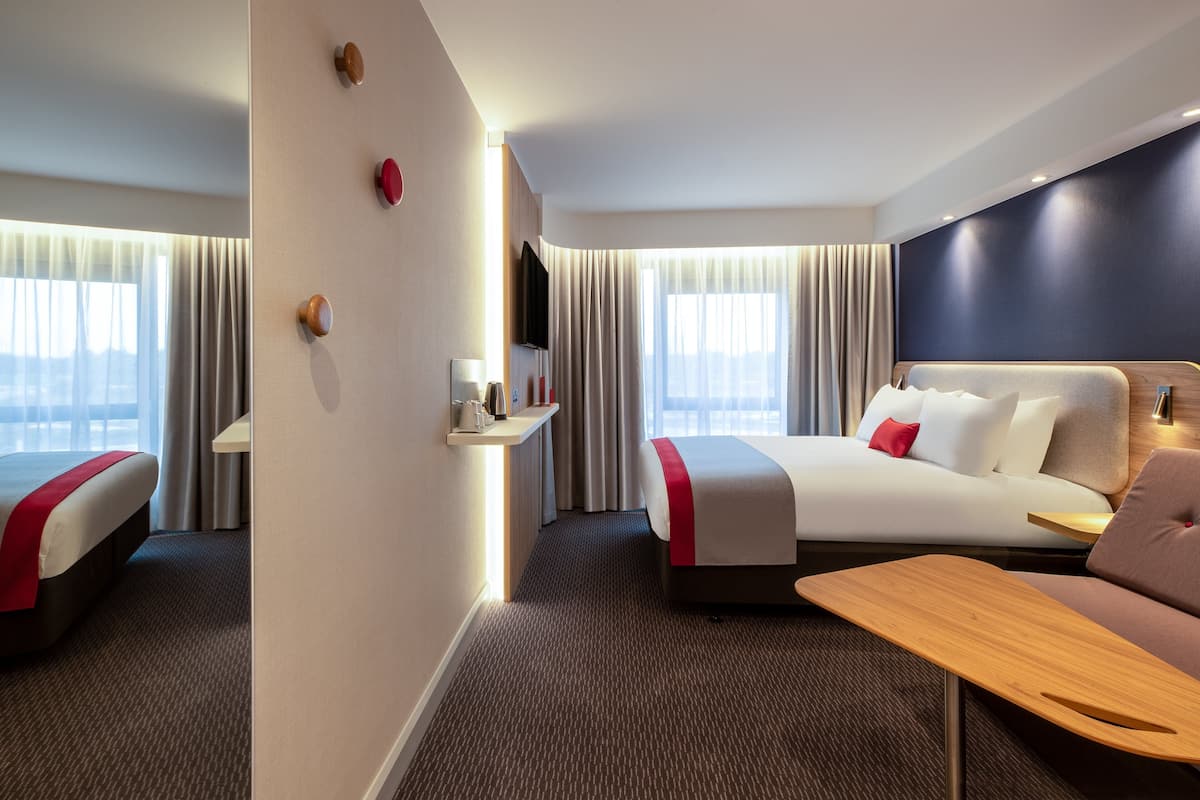 A hotel room with two beds, a TV, a desk, and a view of the city.