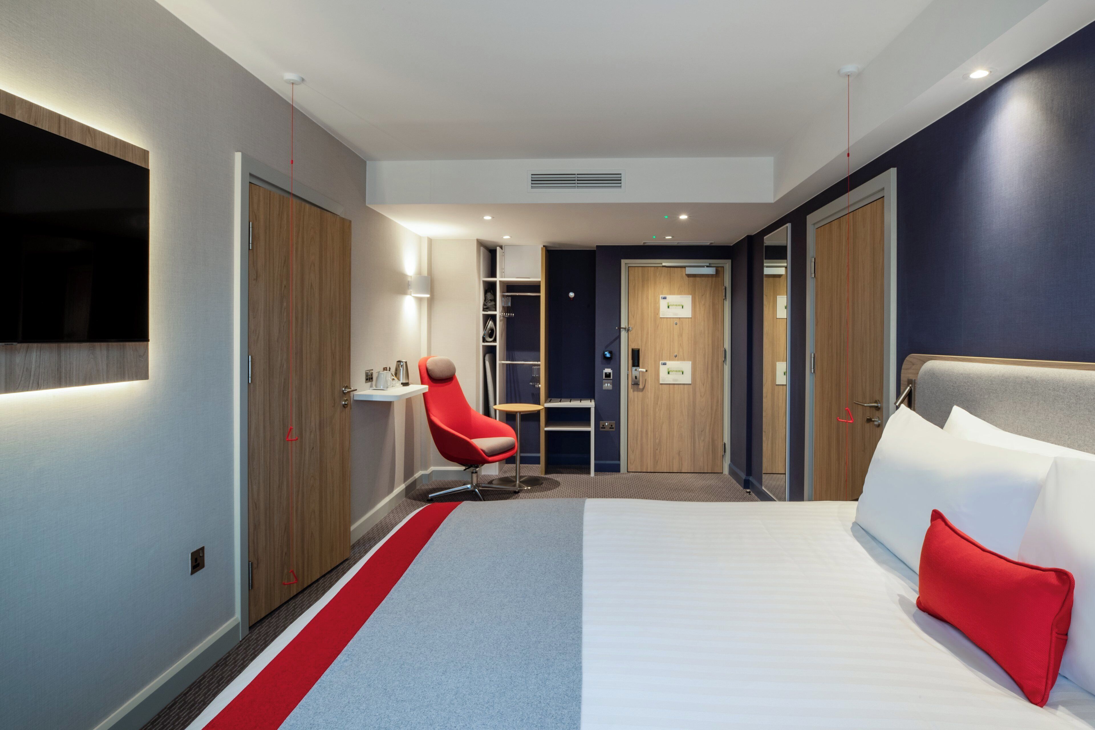 Ein Hotelzimmer mit einem Bett, einem roten Sessel, einem kleinen Tisch und einem Schrank.