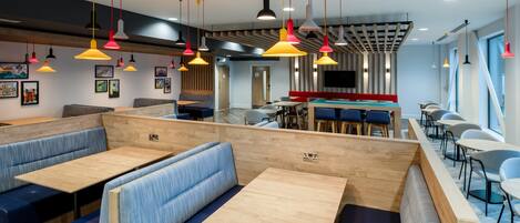 A modern restaurant with booths and tables, colorful pendant lights, and artwork on the walls.