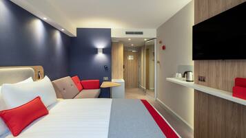A hotel room with a bed, a TV, a small table, and a red accent wall.