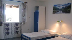 Quarto com duas camas de solteiro, um guarda-roupa, uma janela com cortinas, uma luminária na parede e um quadro emoldurado.