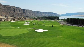 A golf course with bunkers, a water body, and a mountainous backdrop. - Well Appointed Oasis in the Sun! ☀️⚓️🏖 Pool, Beach, Boat Launch, Gorge, Wineries (Quincy)
