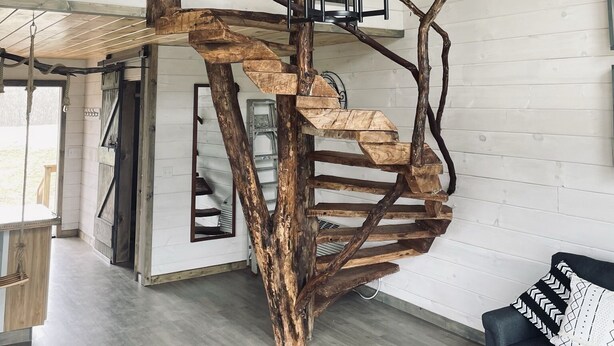 A rustic interior with a wooden tree structure suspended from the ceiling, a ceiling fan, and a modern sofa with patterned cushions. - The "Hang-over"  Winery Treehouse (Weston)