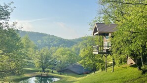 A rustic cabin with a balcony overlooking a lush valley and a small pond. - The "Hang-over"  Winery Treehouse (Weston)