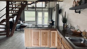 A rustic kitchen with wooden cabinets, a large island, and a staircase leading to a dining area. - The "Hang-over"  Winery Treehouse (Weston)