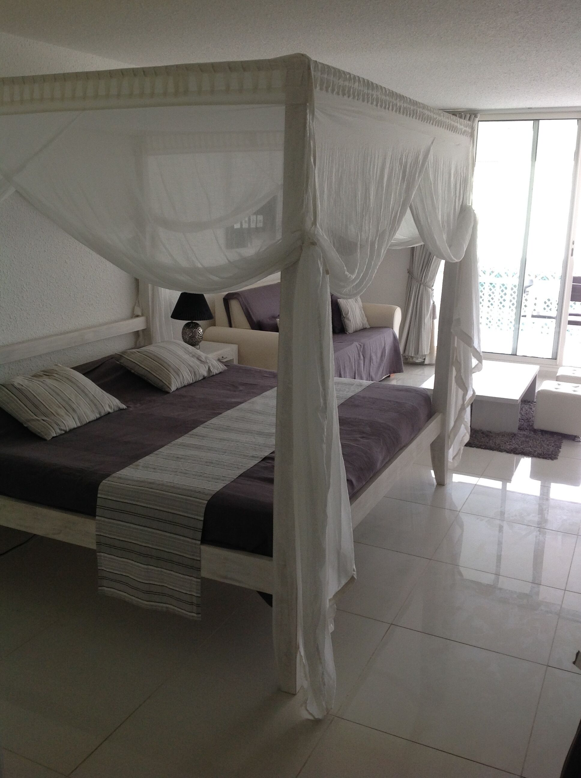 Ein Himmelbett mit weißer Bettdecke und vielen Kissen.