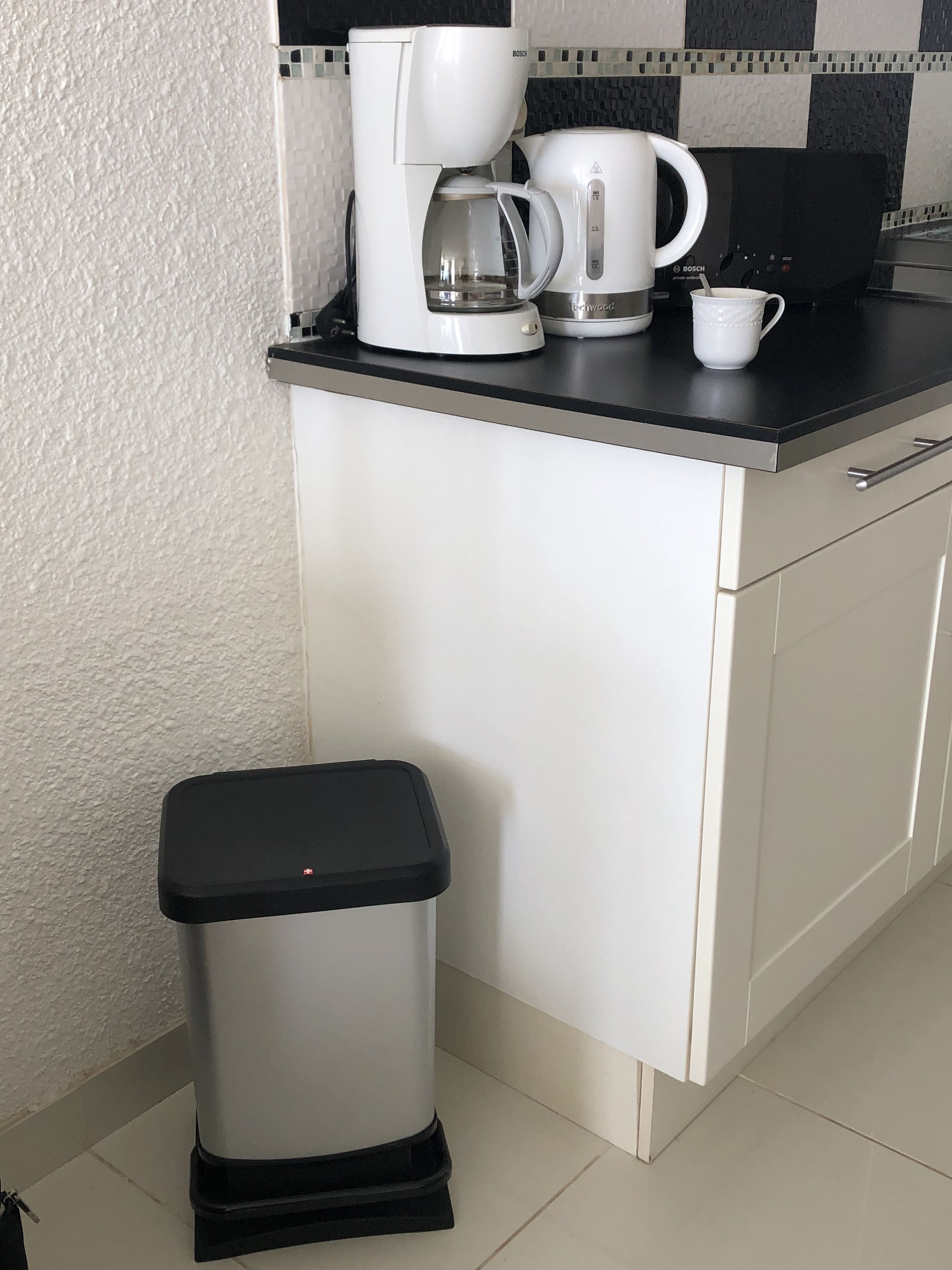 Ett litet kök med en kaffebryggare, en mugg och en papperskorg.