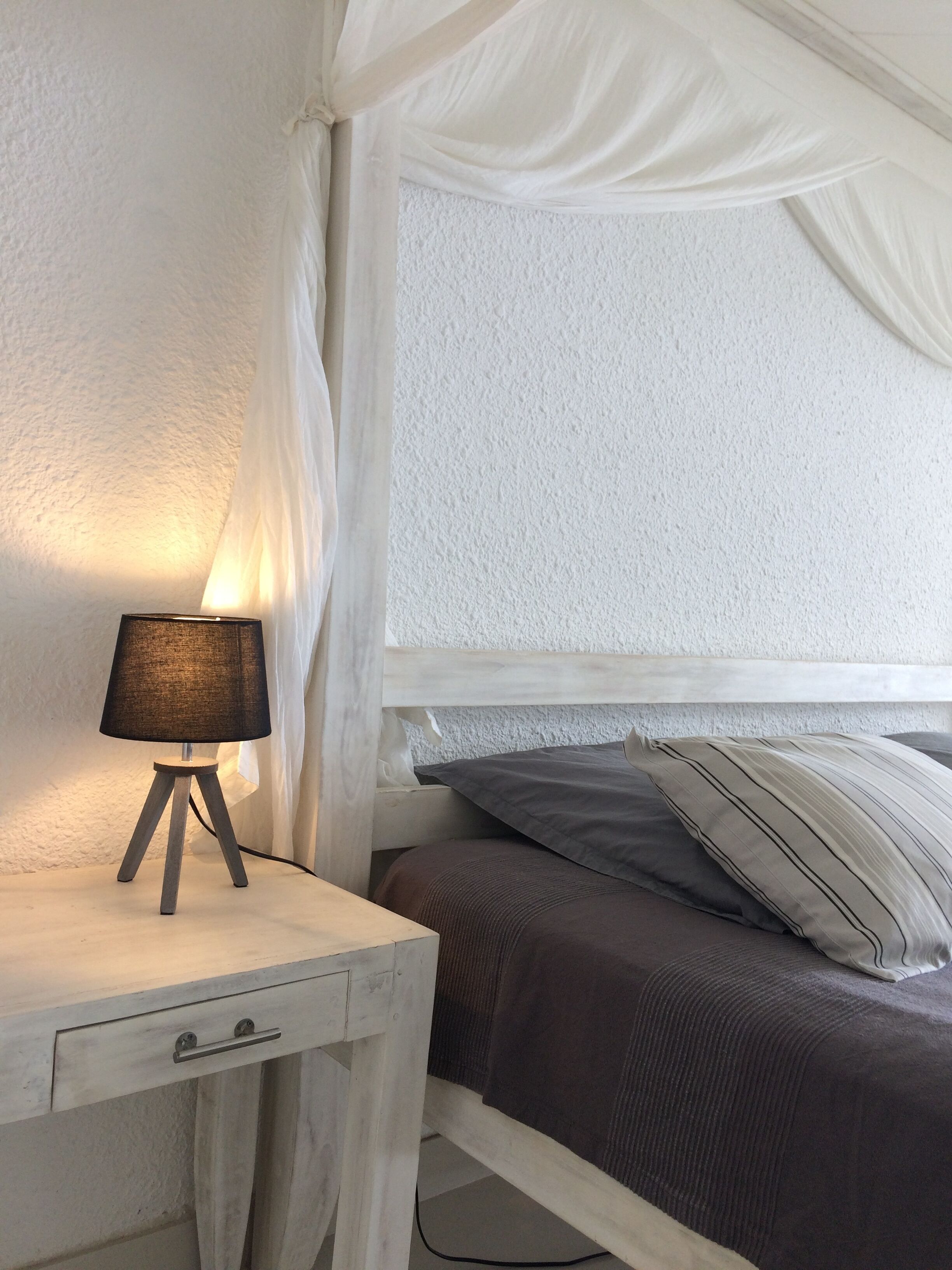 Una camera da letto con un letto bianco, un comodino con una lampada e una tenda.