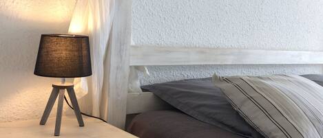 Una camera da letto con un letto bianco, un comodino con una lampada e una tenda.