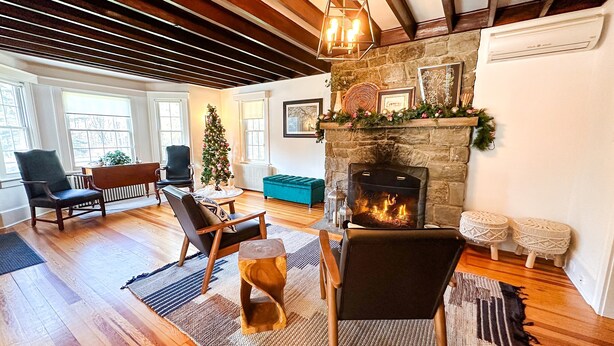 A cozy living room with a stone fireplace, wooden beams, and a Christmas tree.