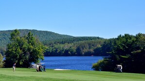 A golf course with a lake and forested hills in the background.