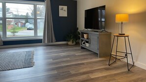 Ein modernes Wohnzimmer mit großem Fenster, einem Flachbildfernseher, einer Stehlampe und einem grauen Schrank mit Dekoration.