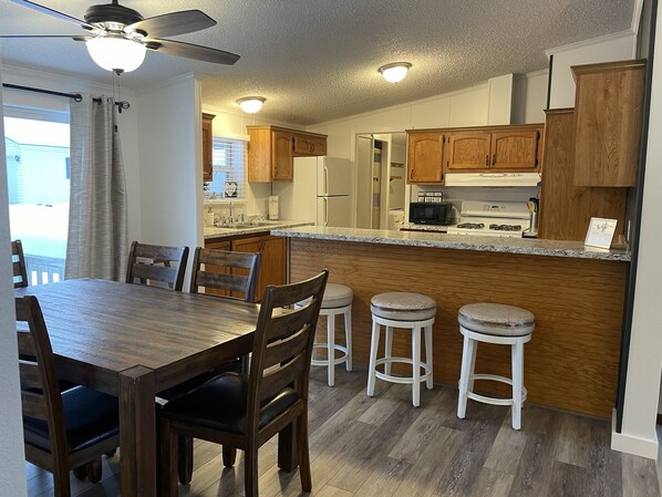 A kitchen with wooden cabinets, a granite countertop, a dining table with chairs, and a ceiling fan.