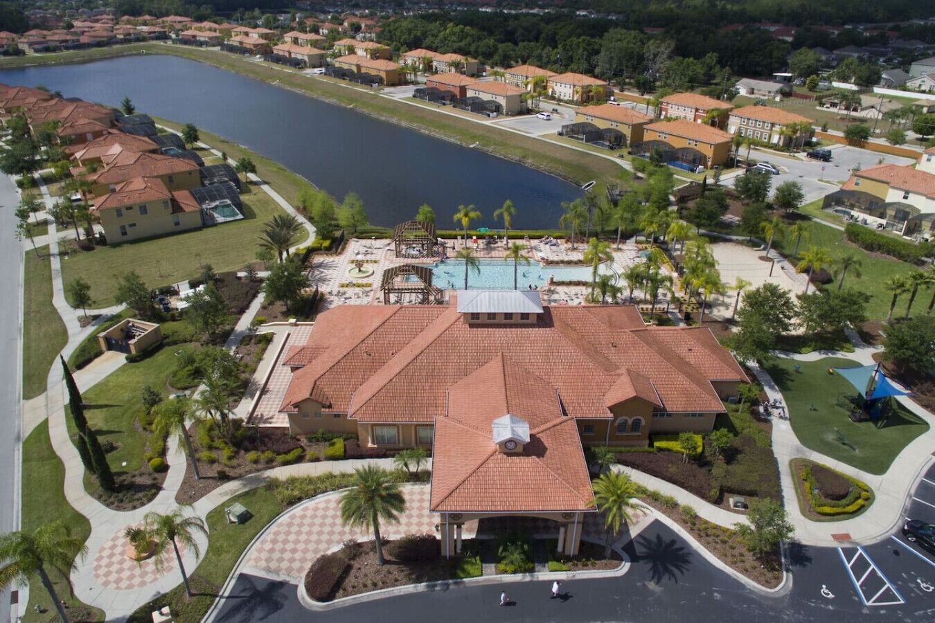 A large building with a red-tiled roof, a swimming pool, and a landscaped area with palm trees.