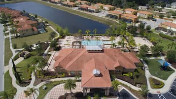 A large building with a red-tiled roof, a swimming pool, and a landscaped area with palm trees.